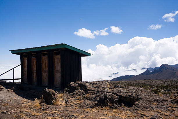 Simple public toilet shelter on the rocky slopes of Mount Kilimanjaro beneath a bright blue sky.